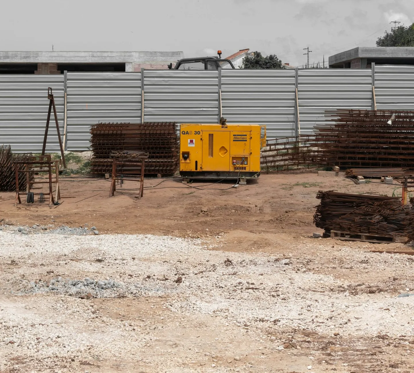 Gerador amarelo em canteiro de obra com vergalhões e tapume ao fundo